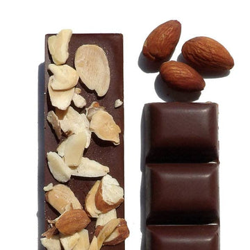 An unwrapped Almond Butter Crunch with Cinnamon Truffles bar, with almonds above the bar.