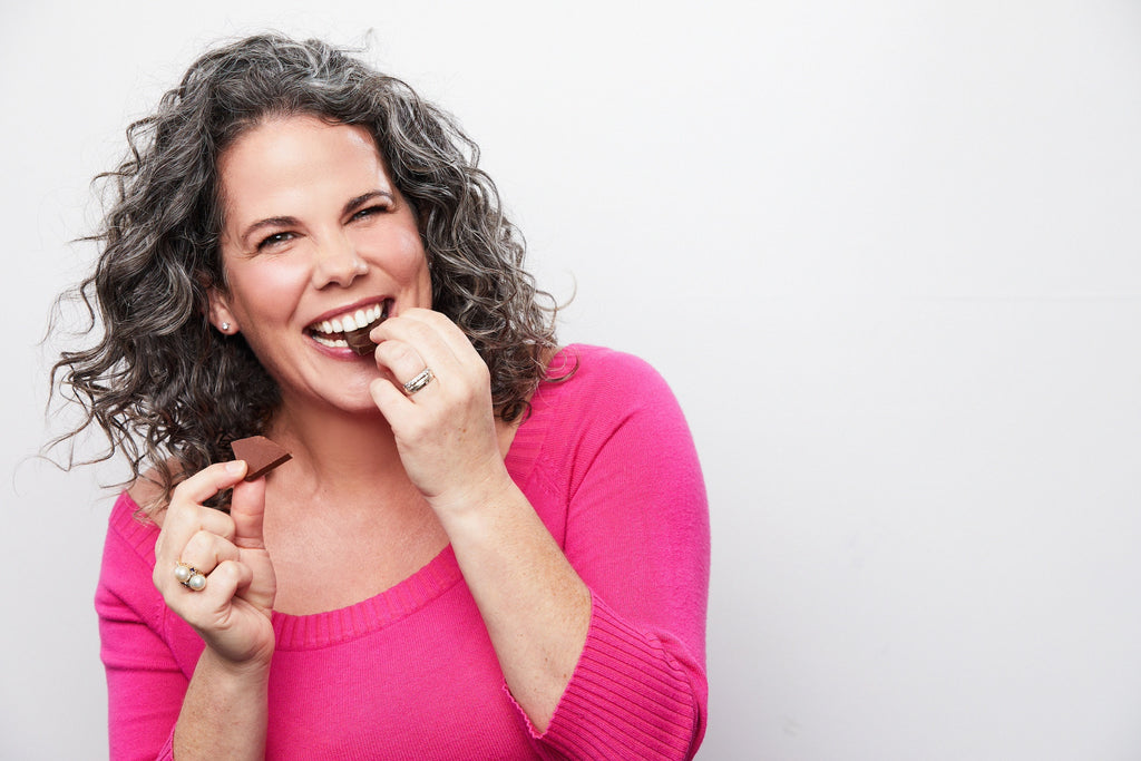 Picture of Founder Kala Maxym in a pink shirt eating chocolate