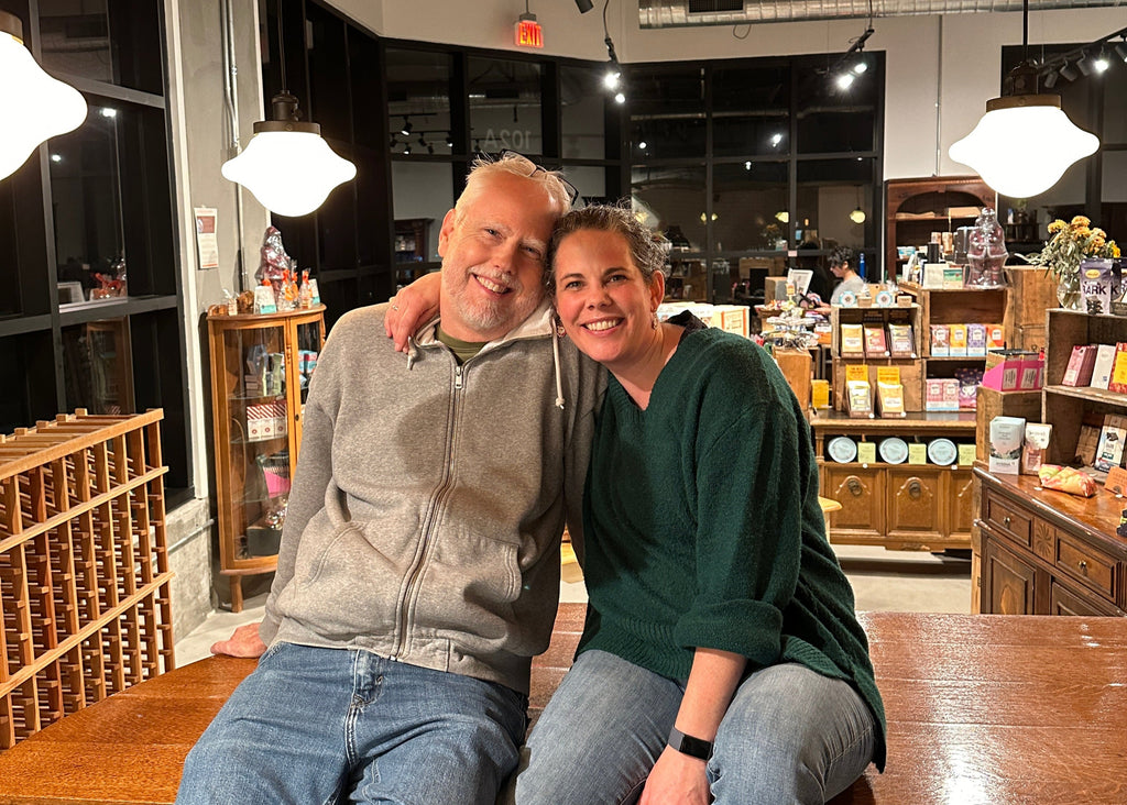 A man and a woman sit atop a wooden bar in a chocolate shop