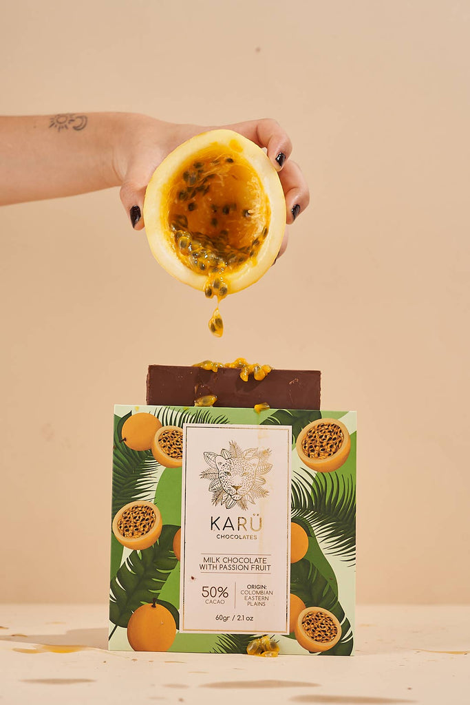 A hand holding a passion fruit above a Milk Chocolate with Passion Fruit 50% bar against a beige background